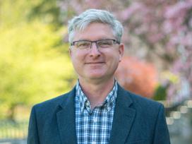 A person with glasses in front of green trees