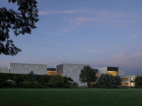View of the new Palmer Museum of Art at dusk from the H.O. Smith Botanic Gardens in the Arboretum at Penn State. Credit: Photo by Jeremy Bittermann/JSBA, courtesy of Allied Works. All Rights Reserved. A white museum building with green grass in the foreground. At dusk.
