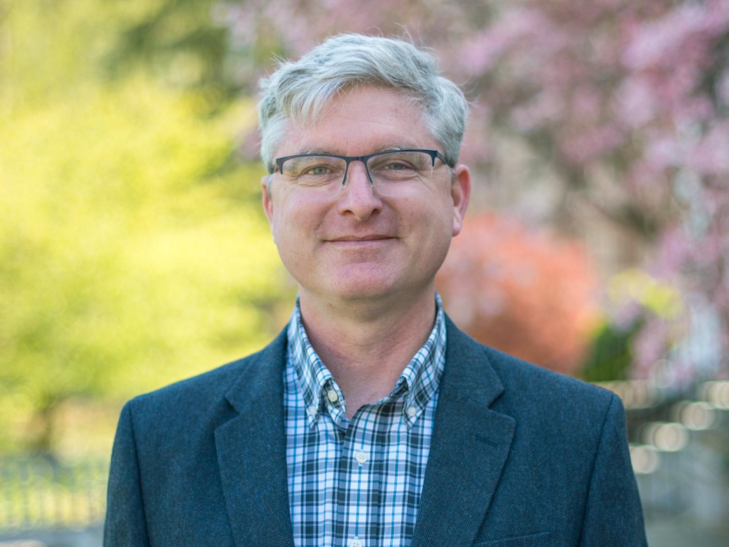 A person with glasses in front of green trees